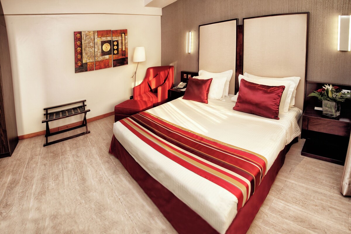 A hotel room with a large bed, a bench, a nightstand, and a wall-mounted artwork.
