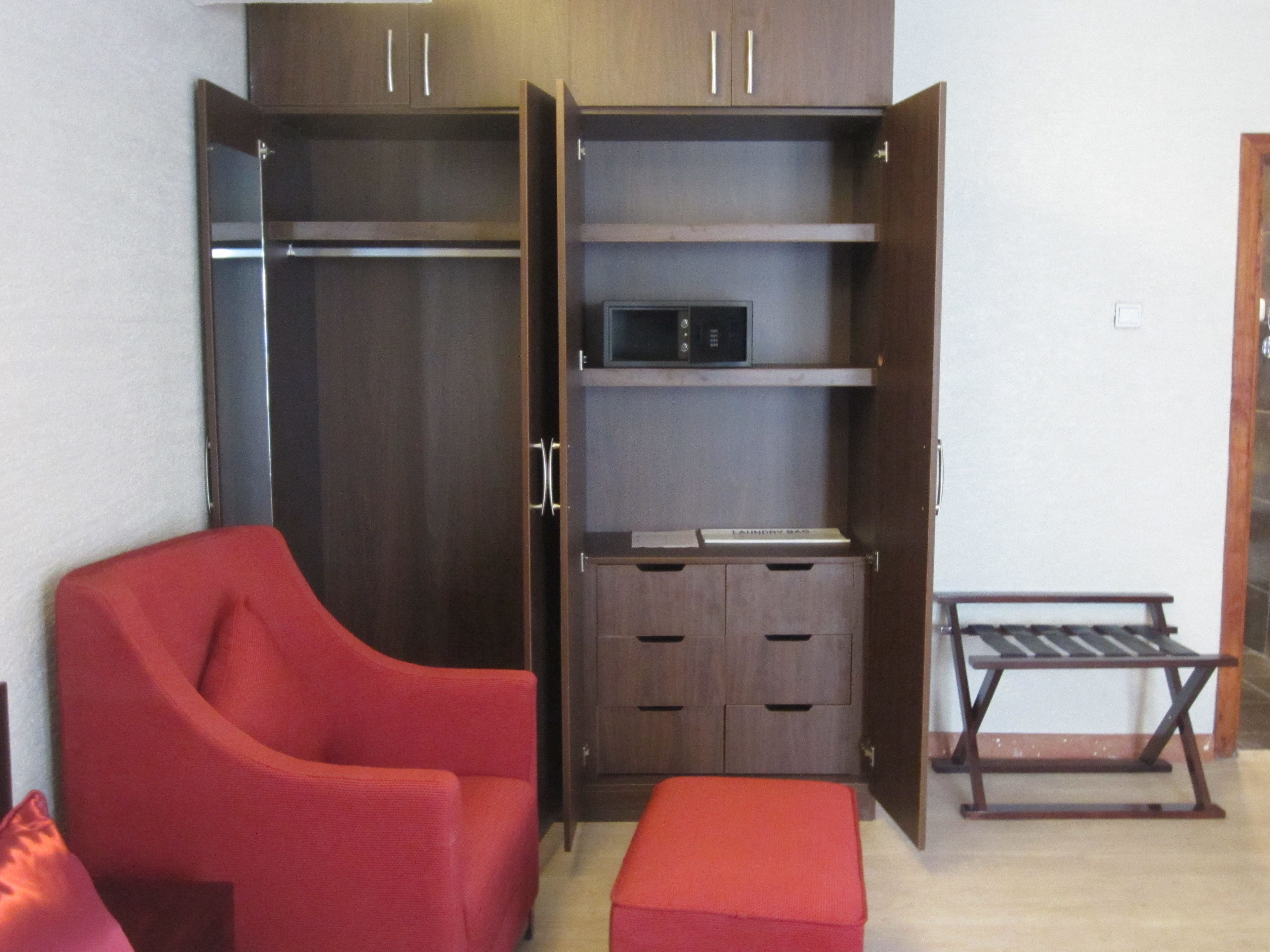 A room with a red armchair, a wooden wardrobe with open doors, a small table, and a bench.