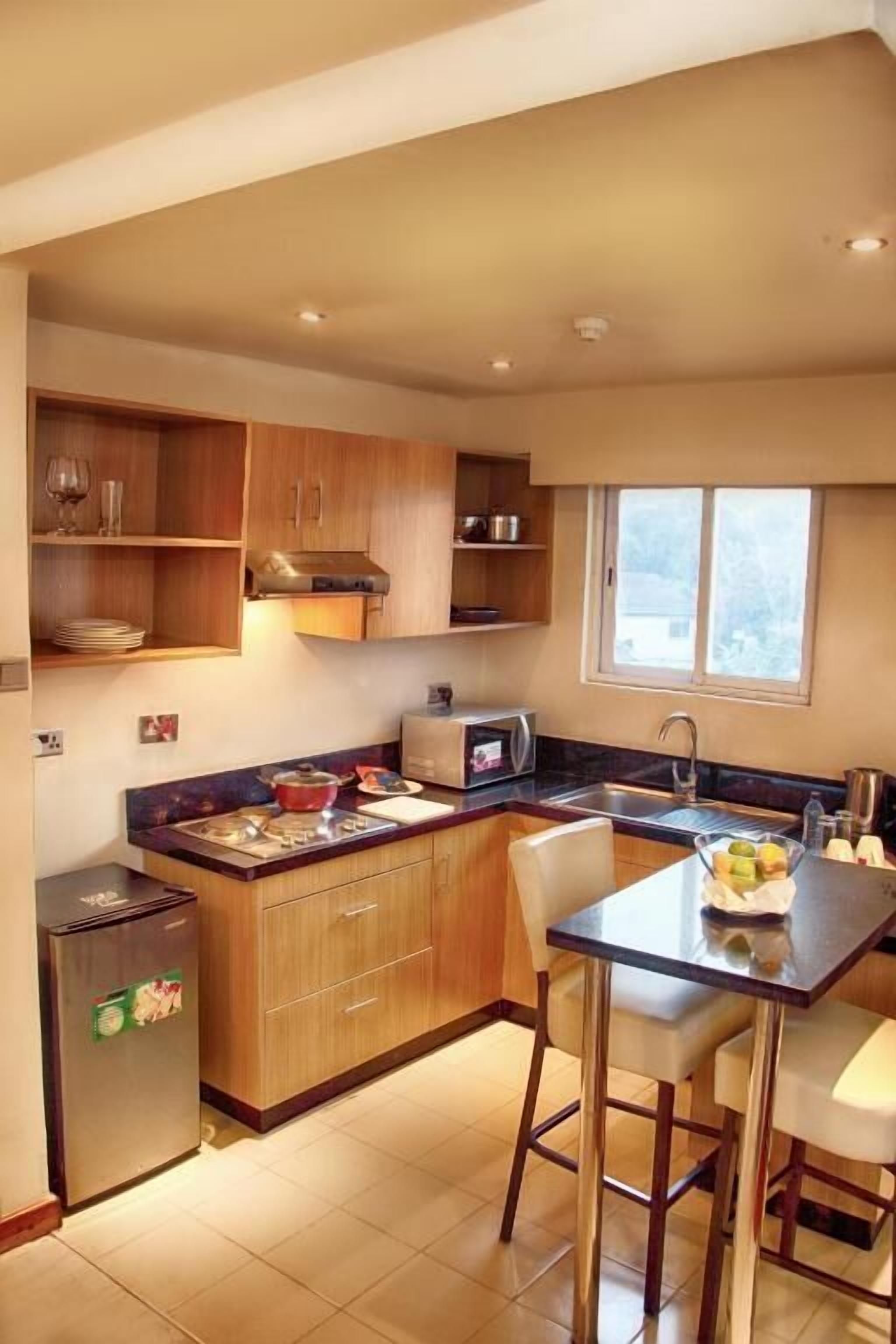 A compact kitchen with wooden cabinets, a built-in microwave, a refrigerator, and a window providing natural light.