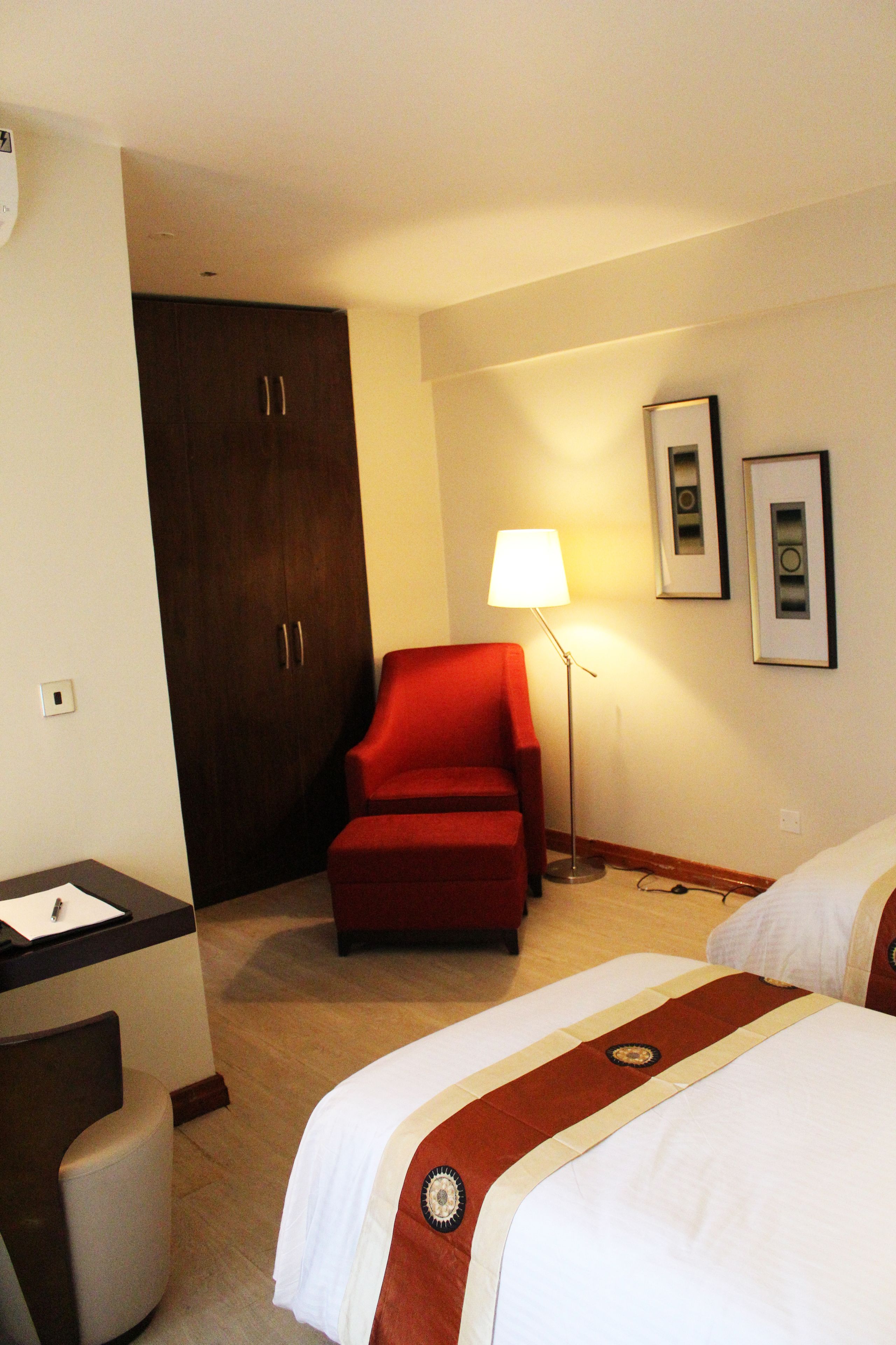 A hotel room with a bed, a desk, a chair, a wardrobe, and a lamp.