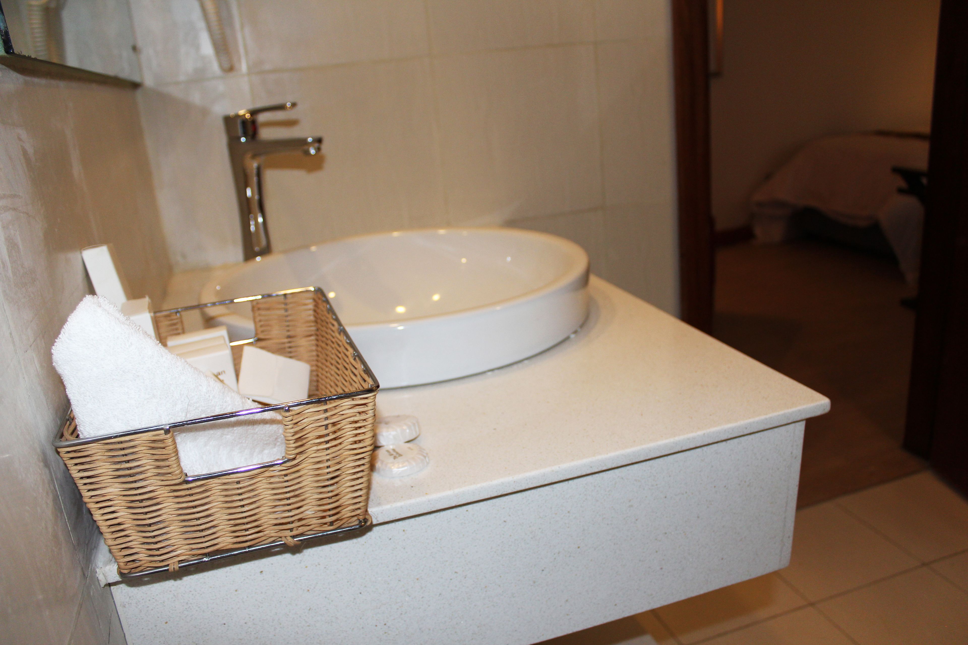 A bathroom with a white sink, a mirror, and a wicker basket with a white towel.