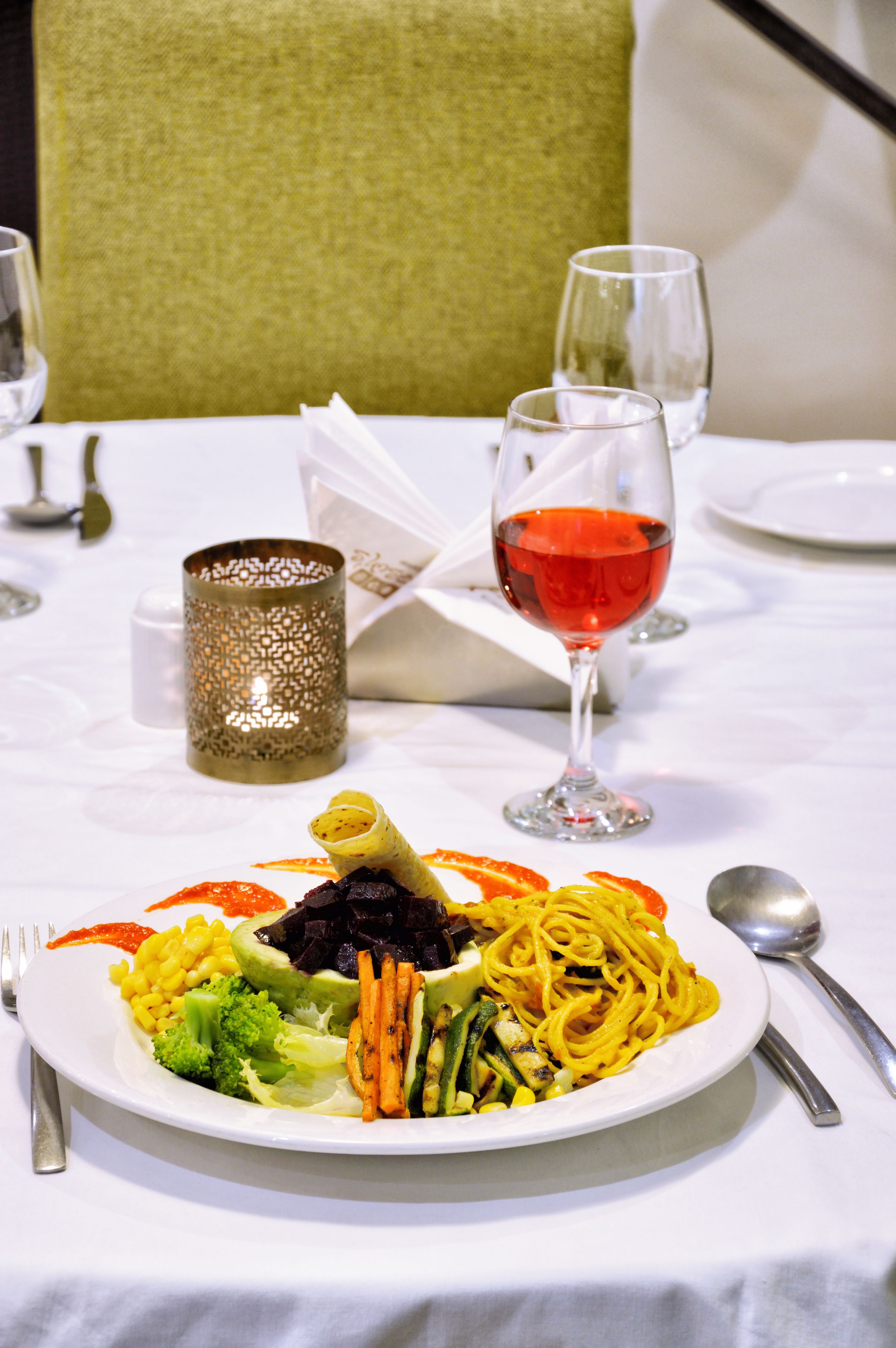A dining table with a plate of food, a glass of red wine, and a decorative candle.