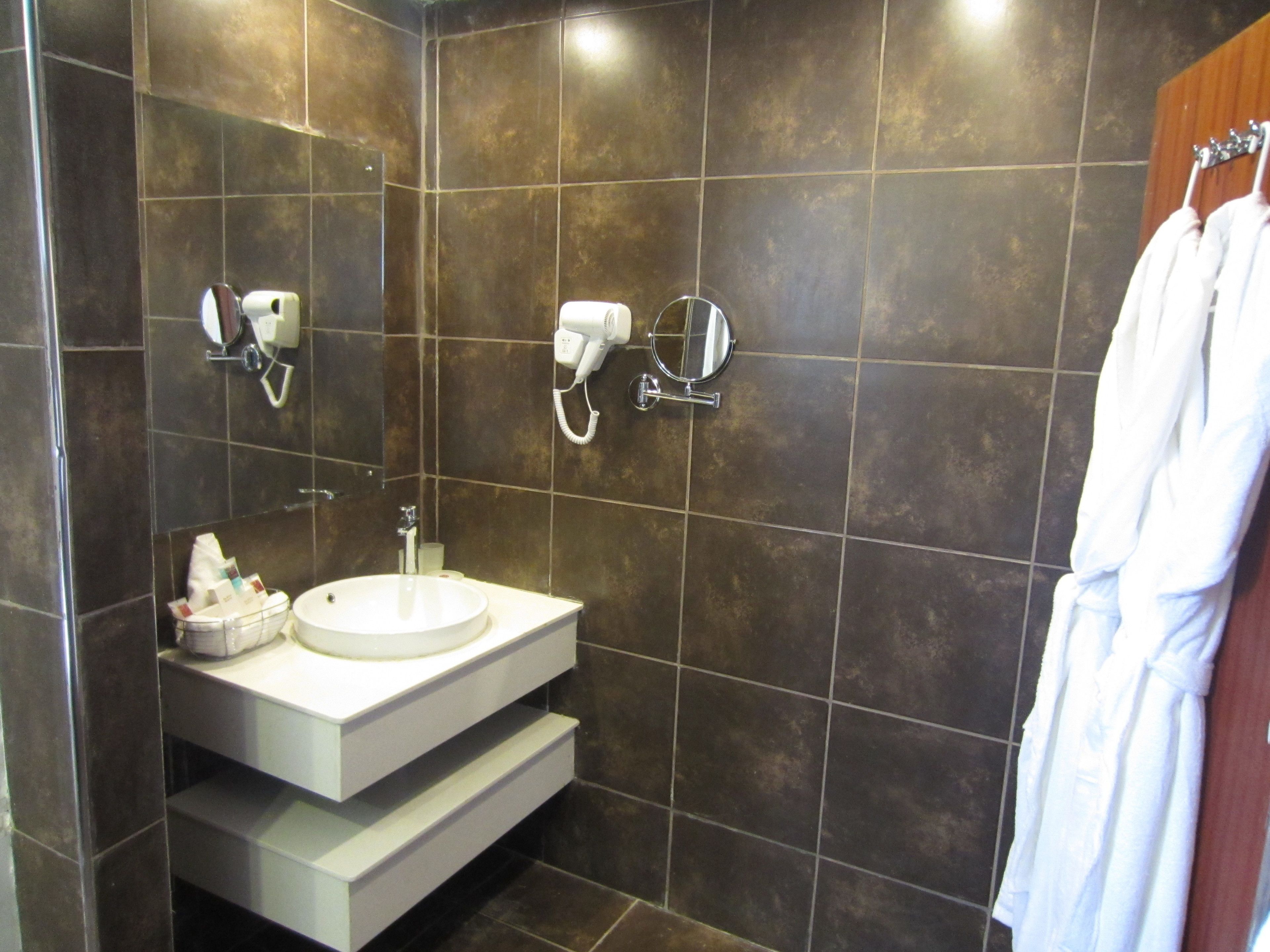 A modern bathroom with a white sink, a mirror, and a hairdryer mounted on the wall.
