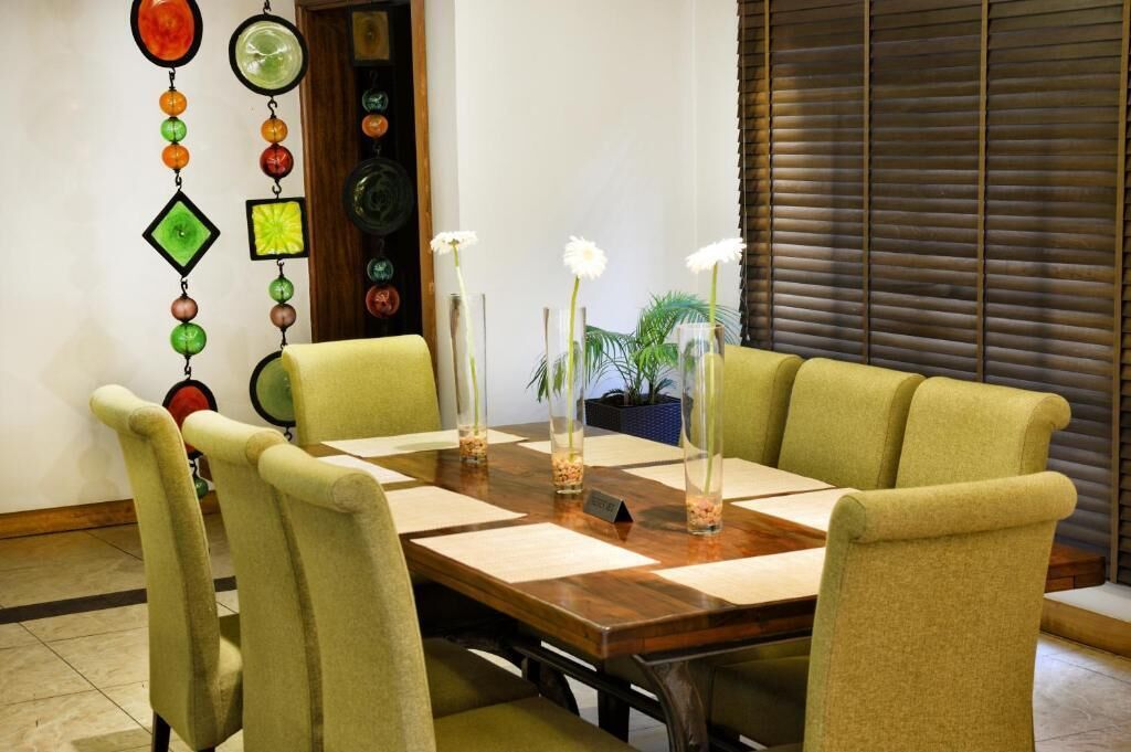 A conference room with a wooden table, green upholstered chairs, and decorative glass vases with white flowers.
