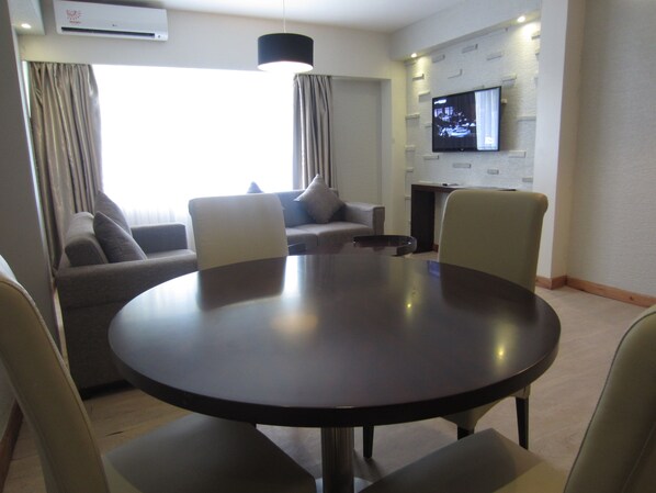 A modern living room with a round table, two sofas, and a flat-screen TV mounted on the wall.