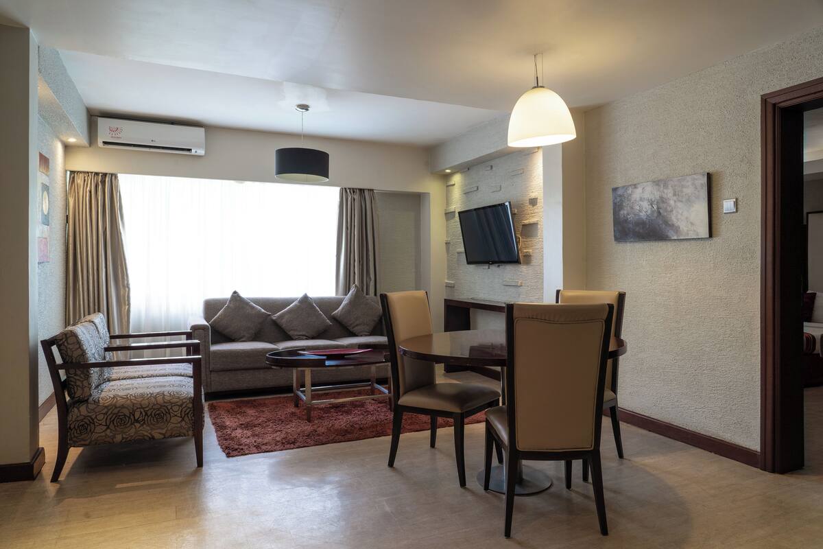 A modern living room with a sofa, chairs, a dining table, and a TV mounted on the wall.