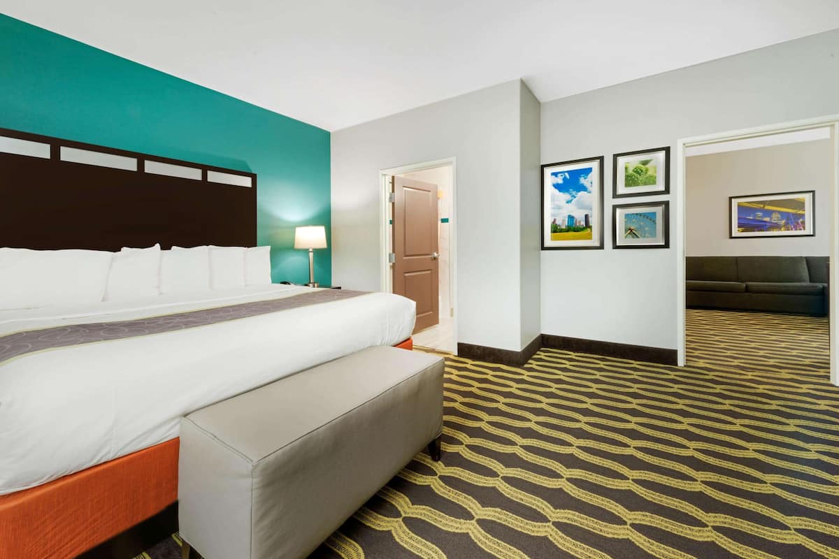Une chambre d’hôtel avec un lit, un banc, une lampe, une porte et un tapis à motifs.