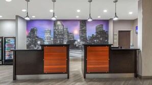 Un espace d’accueil avec deux comptoirs de réception en bois, une fresque murale représentant un paysage urbain et un distributeur automatique en arrière-plan.