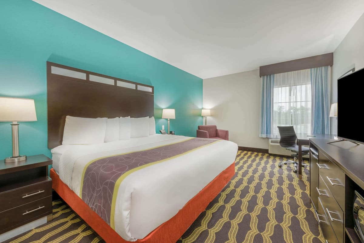 Une chambre d’hôtel avec un grand lit, deux lampes de chevet, un bureau avec une chaise, une télévision et une fenêtre avec des rideaux.