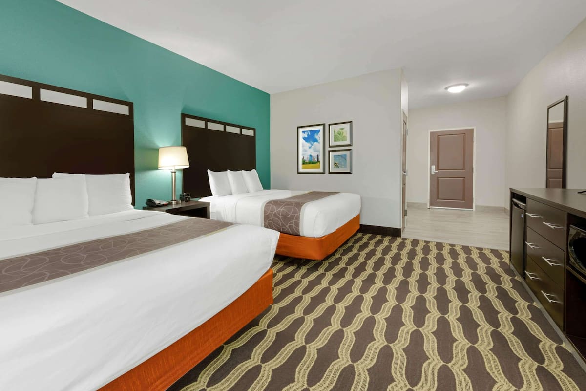 Une chambre d’hôtel avec deux lits, une table de chevet, une lampe, une commode et une porte.