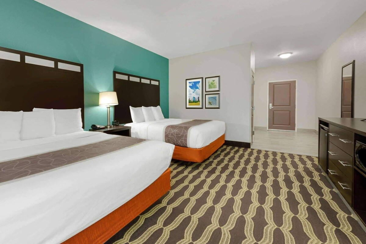 Een hotelkamer met twee bedden, een bureau, een lamp en een deur naar een andere kamer.