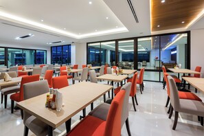 A modern dining area with multiple tables and chairs, large windows, and a bright interior. - Riche Hua Hin (Hua Hin)