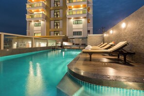 A swimming pool with lounge chairs and a building with multiple balconies in the background.