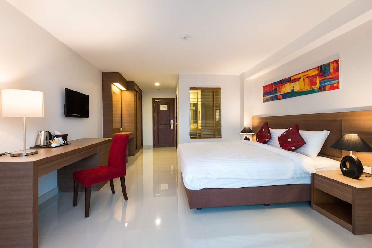 Quarto de hotel moderno com cama, escrivaninha, cadeira e televisão.