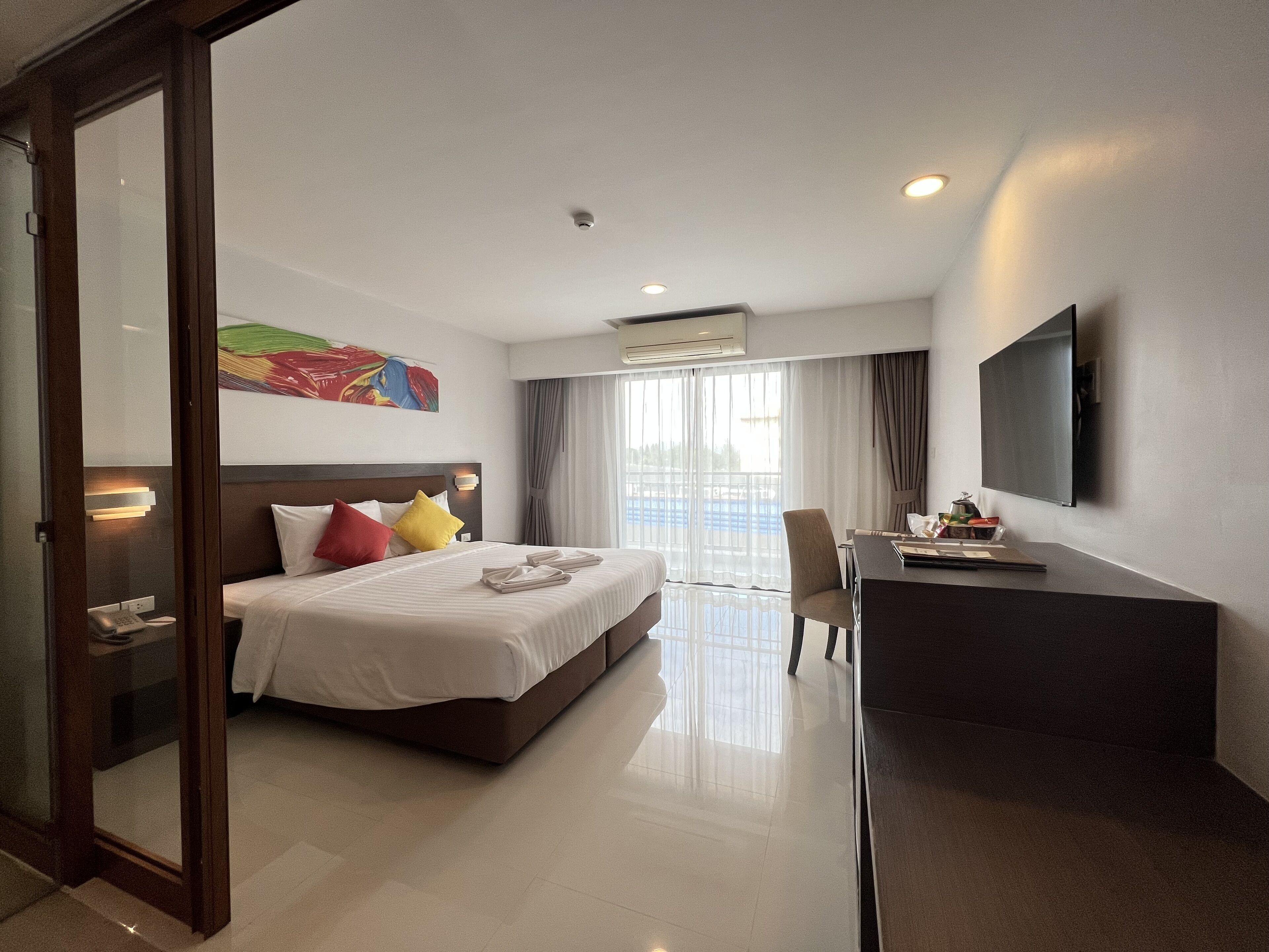 A hotel room with a bed, a desk, a chair, a TV, and a window with curtains.