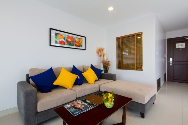 A modern living room with a grey sofa, blue and yellow cushions, a framed floral artwork, a vase with flowers, and a wooden coffee table.