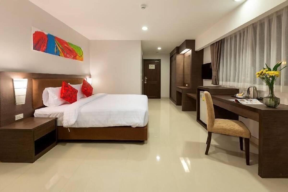 Une chambre d’hôtel comprenant un lit, une table de chevet, un bureau, une chaise et une grande fenêtre avec des rideaux.