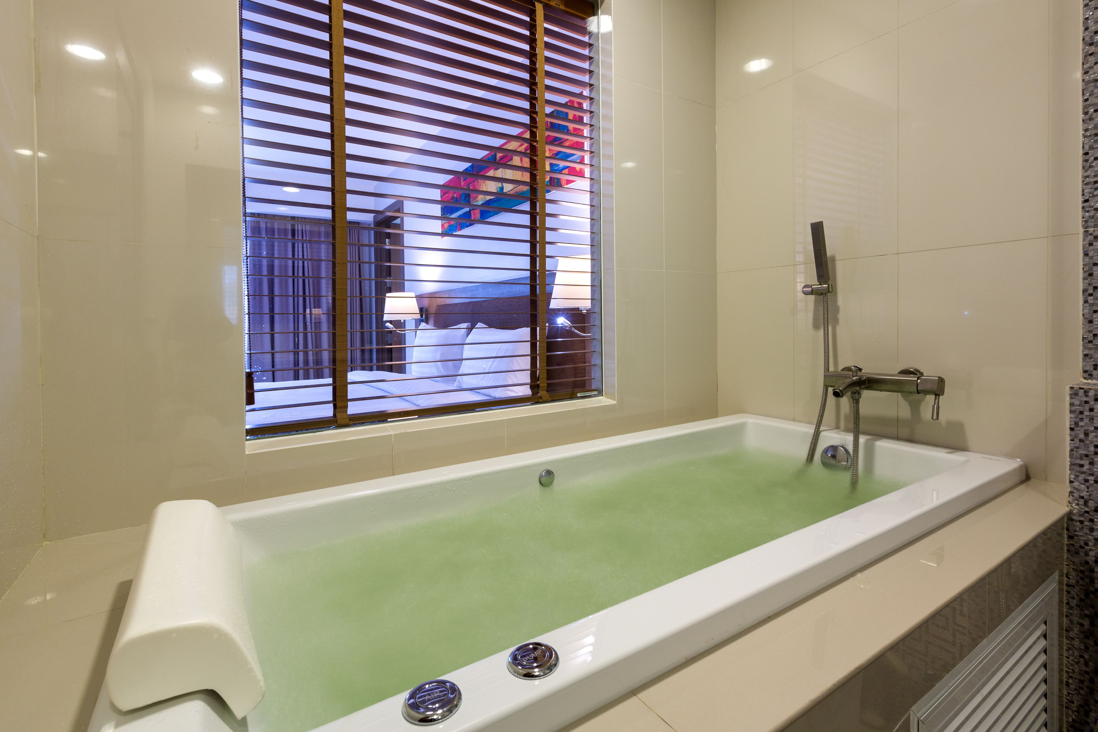 Une salle de bain moderne dotée d’une grande baignoire, d’une douche et d’une fenêtre avec des stores.
