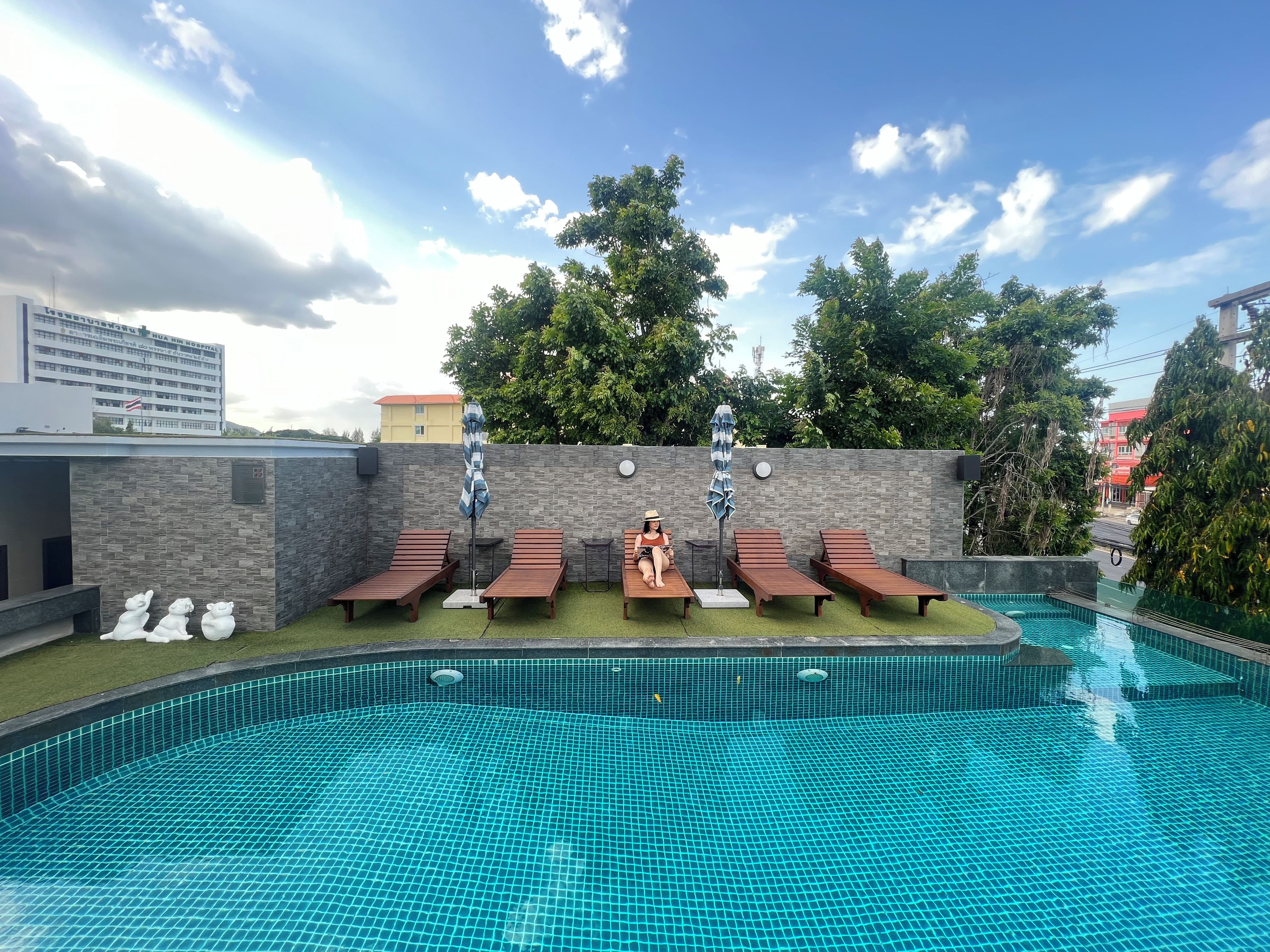 A swimming pool with lounge chairs and a person sitting on one.