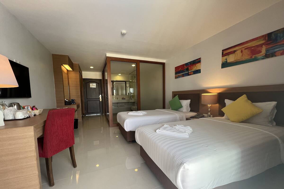 Une chambre d’hôtel avec deux lits, un bureau, une chaise, une télévision et une salle de bain visible à travers une porte ouverte.
