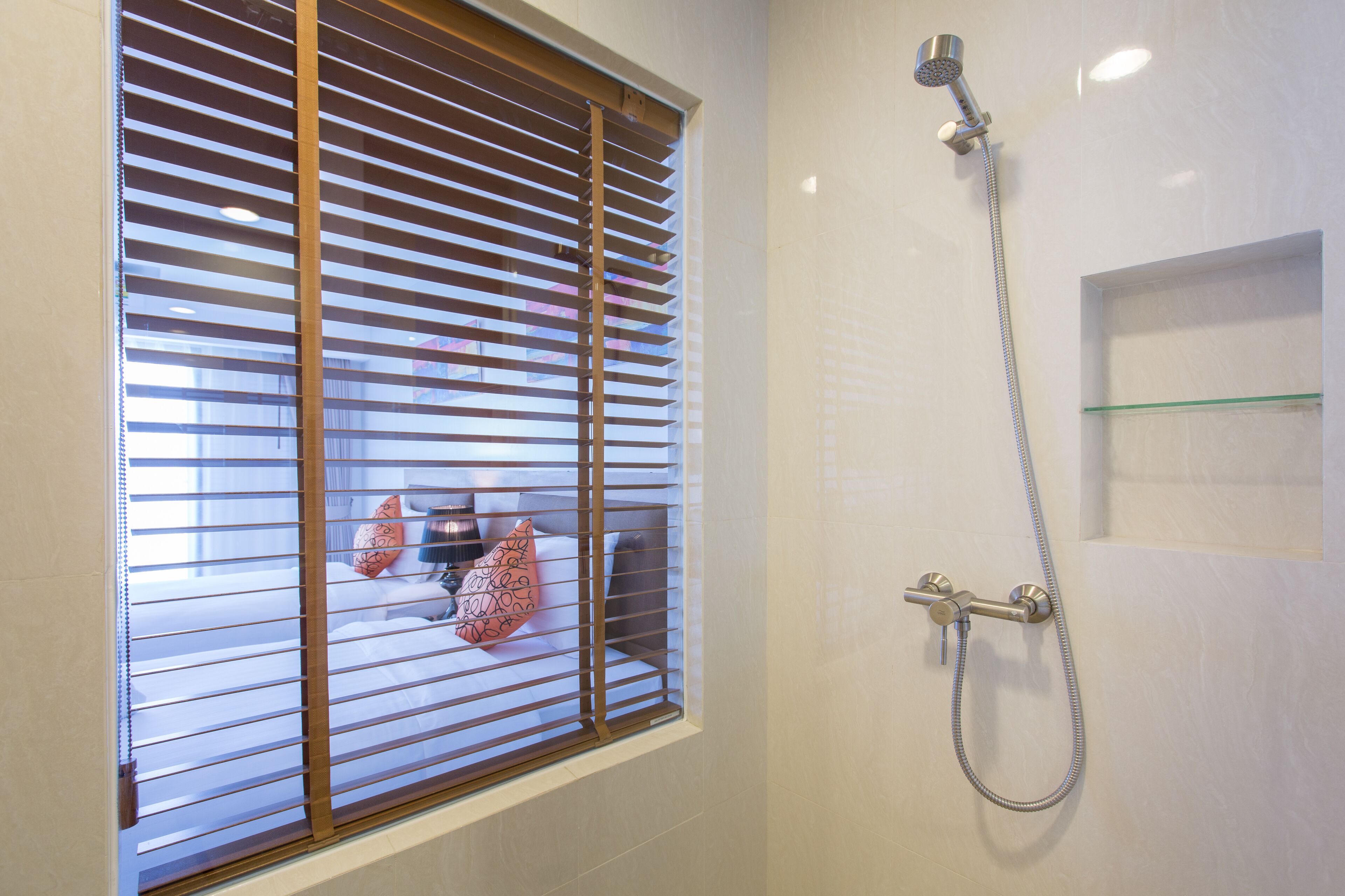 A bathroom with a shower, a window with blinds, and a small shelf.