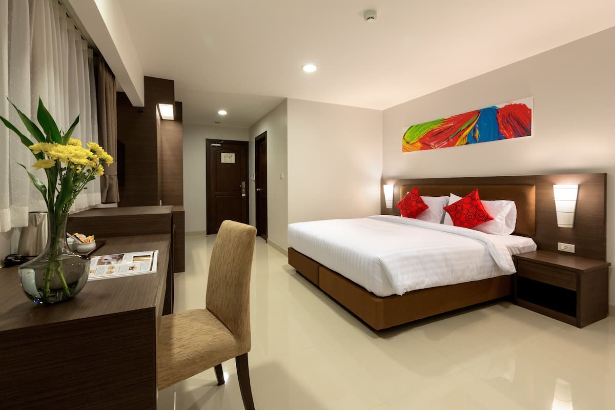 Une chambre d’hôtel moderne avec un grand lit, des tables de chevet, un bureau avec une chaise et un vase de fleurs.