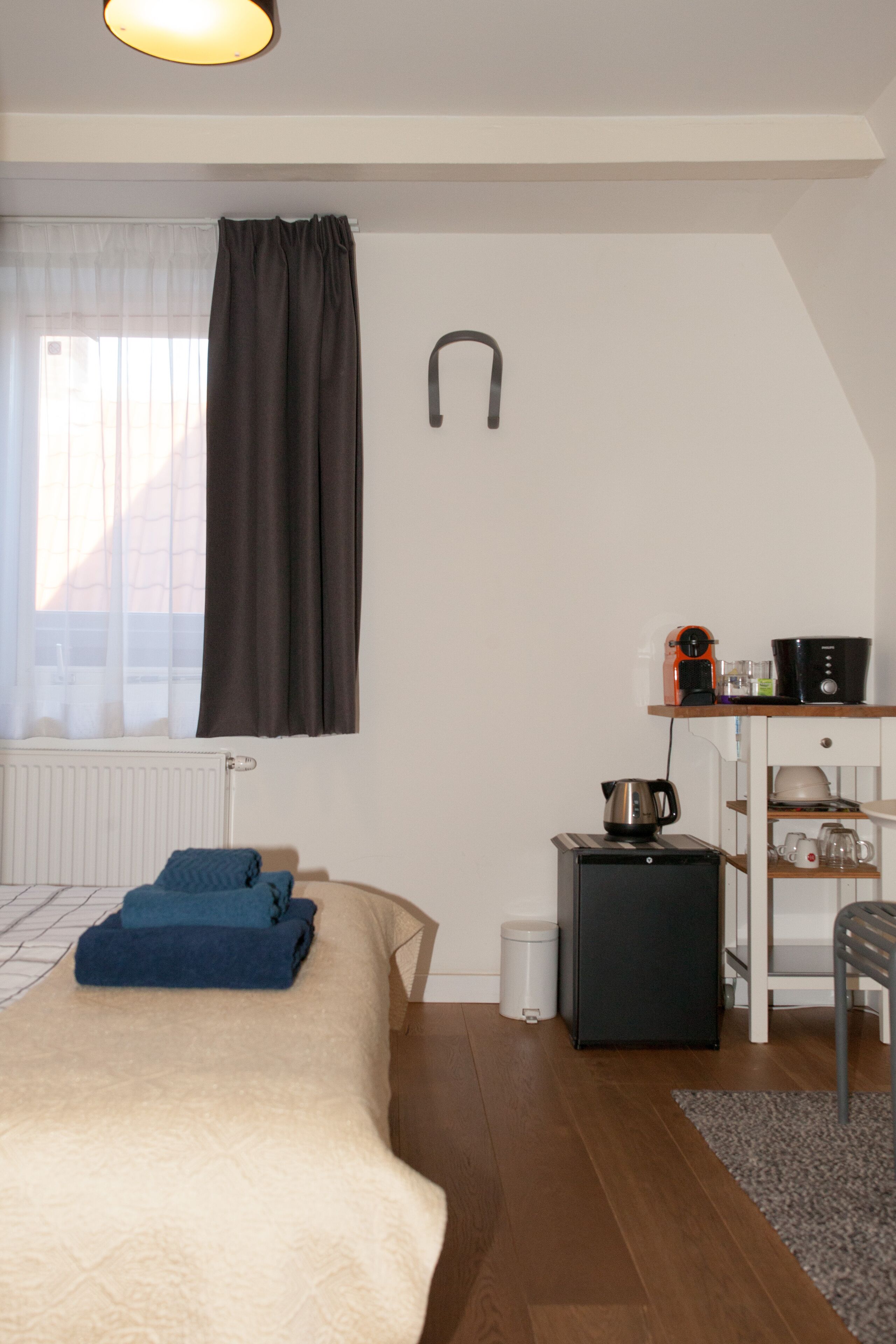 A bedroom with a bed, a radiator, a kettle, a coffee machine, and a small cabinet.
