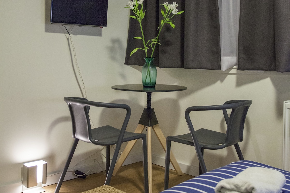 A hotel room with a bed, two chairs, a small table, a TV, and a window with curtains.