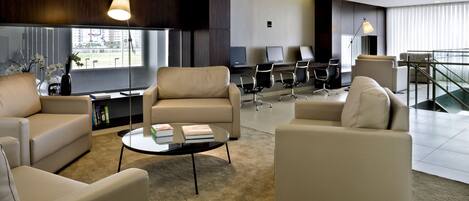 A modern hotel lobby with leather sofas, a coffee table, and a seating area with chairs.