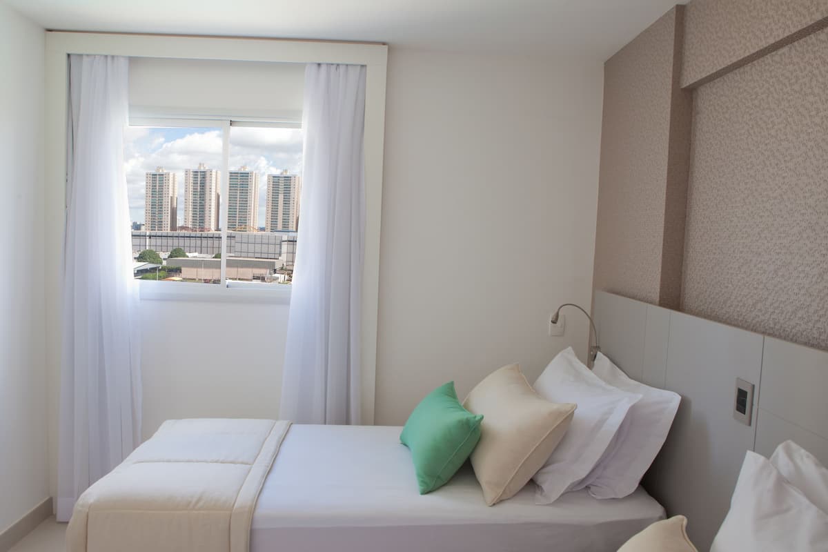 A hotel room with a bed, a window with curtains, and a view of tall buildings.
