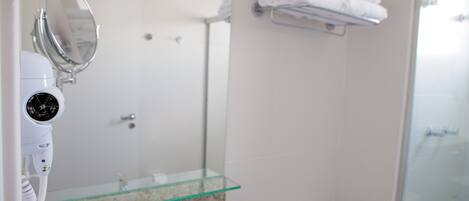 A bathroom with a glass shower enclosure, a white toilet, and a glass sink with a towel rack above.
