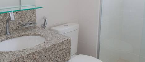A bathroom with a granite countertop sink, a toilet, and a glass shower enclosure.