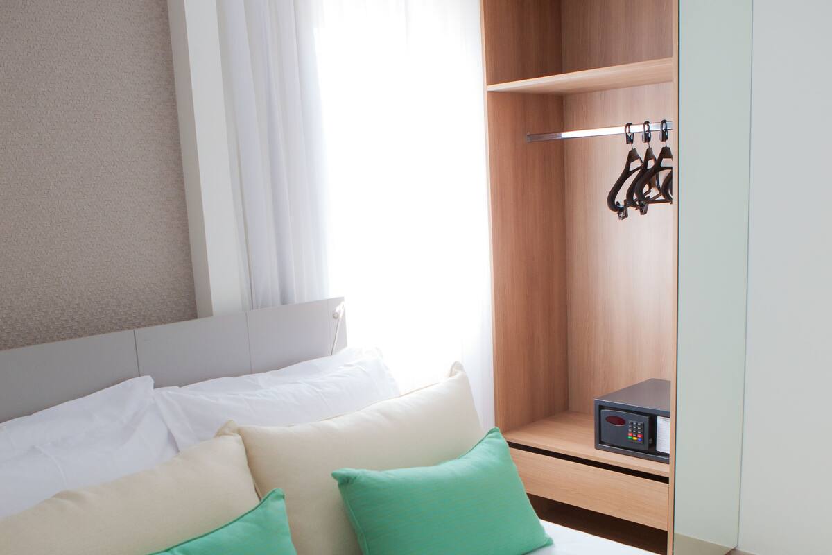 A hotel room with a bed, pillows, a wardrobe, and a small table.