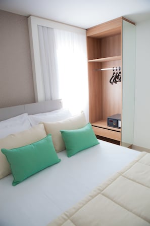 Quarto de hotel com cama, almofadas, um guarda-roupa e uma pequena mesa.