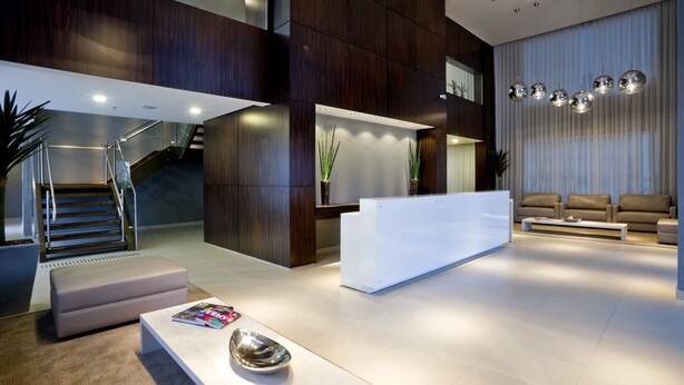 A modern lobby with a reception desk, seating area, staircase, and decorative lighting.