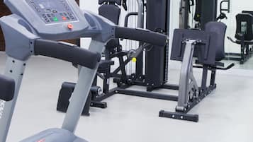 Uma academia com esteira, aparelhos de musculação e espelho.