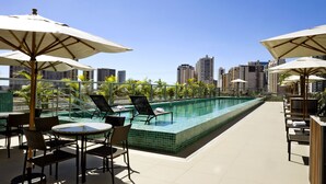 A rooftop pool area with lounge chairs and umbrellas, surrounded by city buildings.