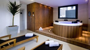 A modern spa room with wooden paneling, a hot tub, and a massage table.