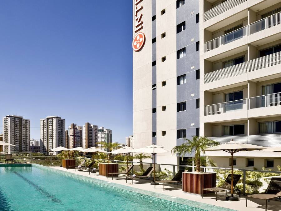 A hotel with a swimming pool, outdoor seating, and a view of the city skyline.