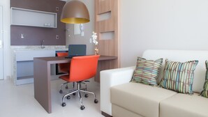 A modern living room with a white sofa, orange office chair, and a desk with a computer.