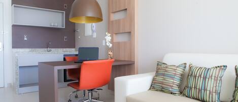 A modern living room with a white sofa, orange office chair, and a desk with a computer.