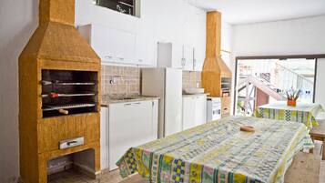 Cocina compacta con horno integrado, armarios blancos y comedor con mesa y bancos.