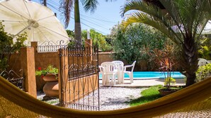 A hammock, a pool, and a garden with chairs and plants. - Pousada Don Pablo (Bombinhas)