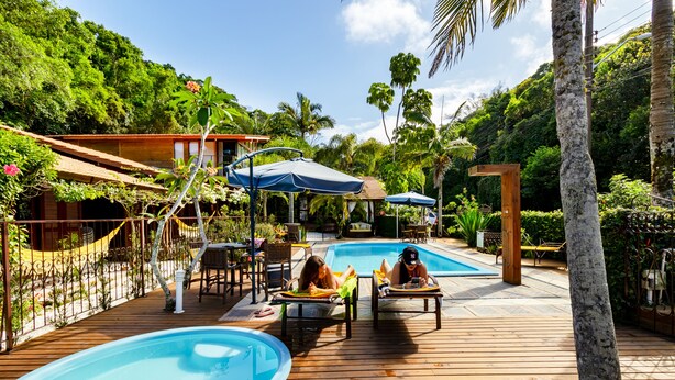 A wooden deck with a pool, lounge chairs, and umbrellas. - Pousada Don Pablo (Bombinhas)
