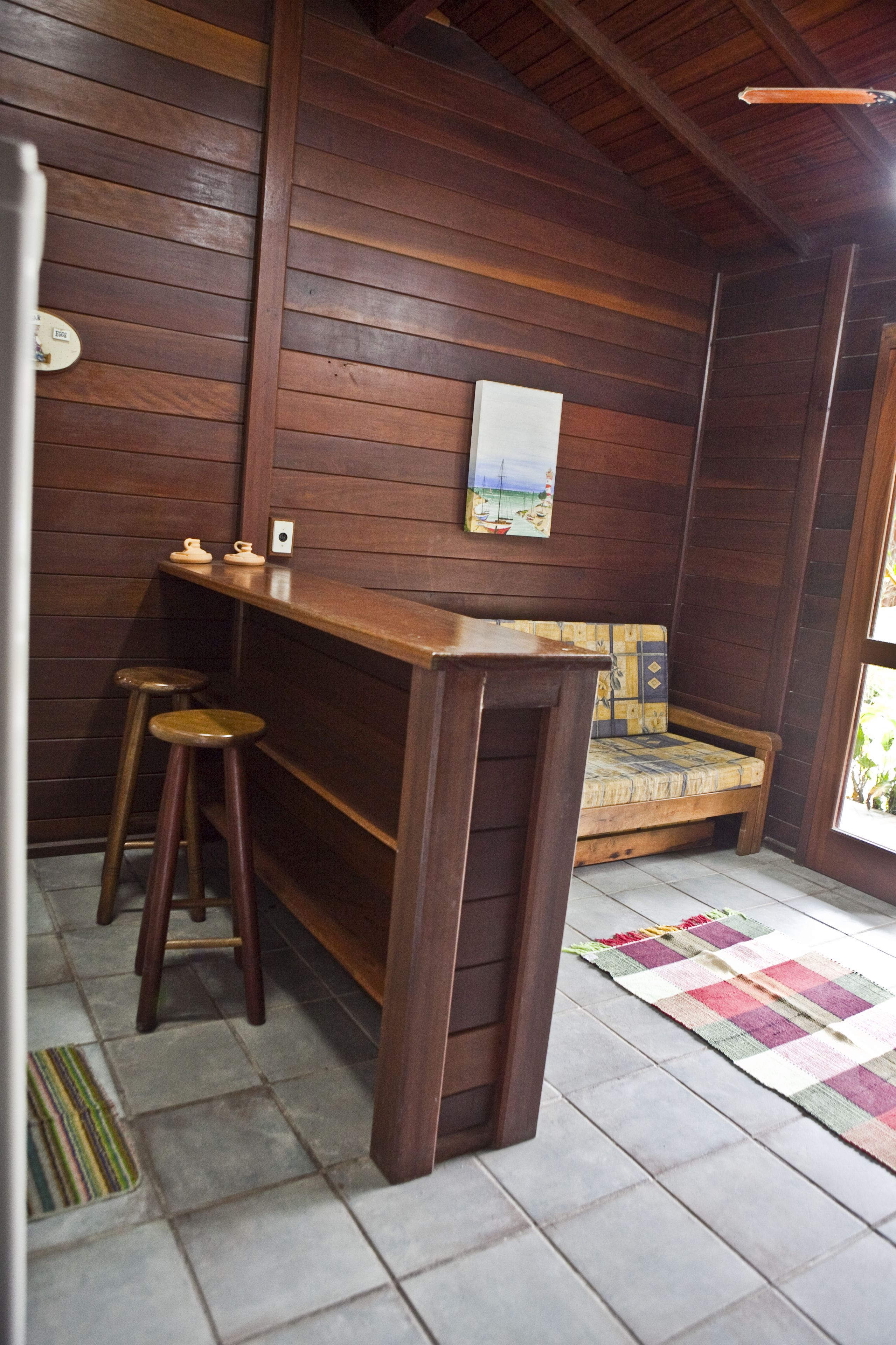 A wooden bar area with stools, a bench, and a painting on the wall.