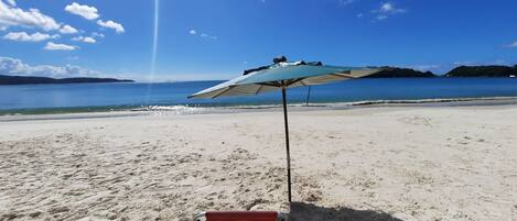 A beach with two red chairs and a blue umbrella.