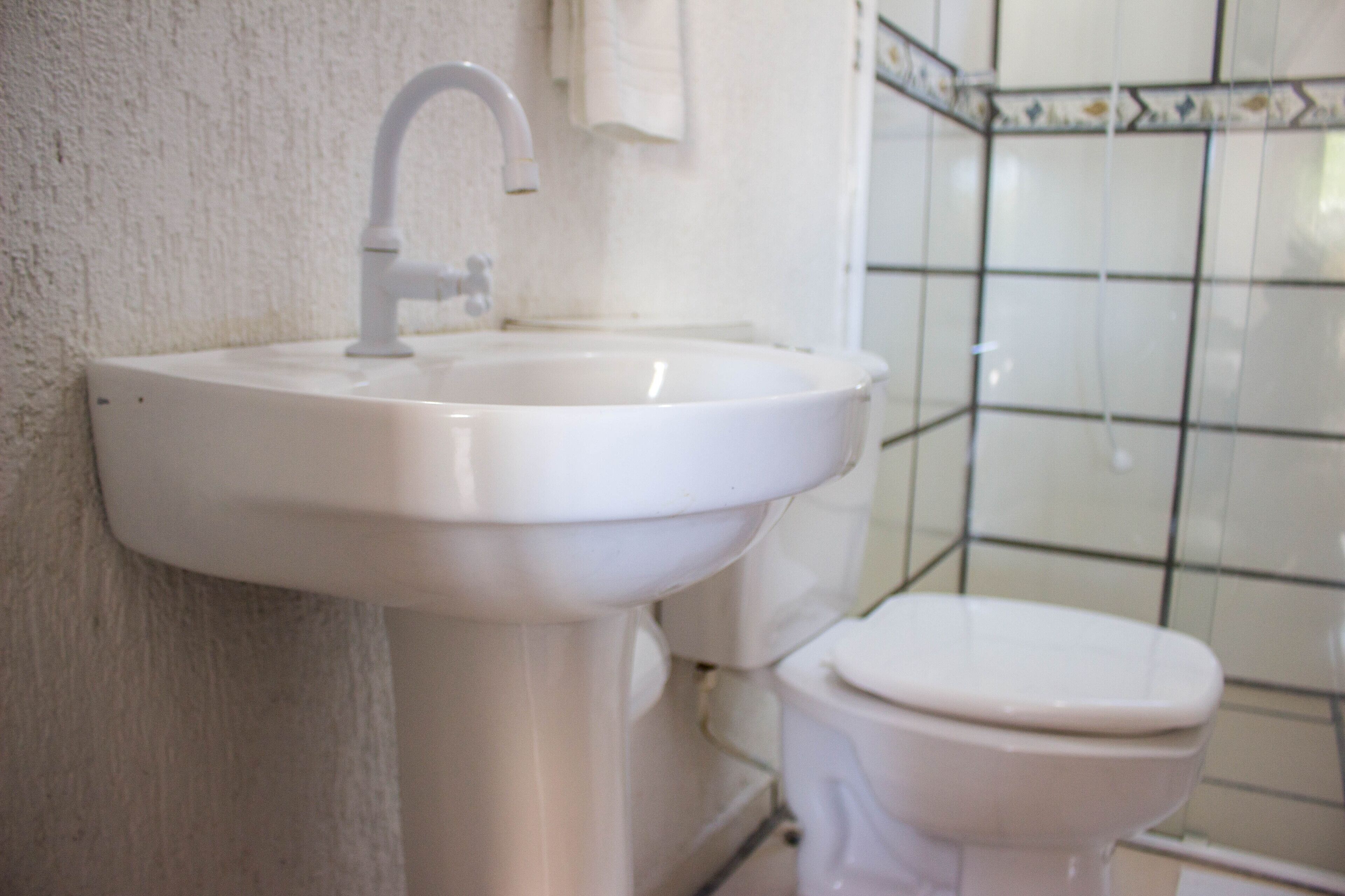 A bathroom with a white sink and toilet, tiled walls, and a visible towel hanging on the wall.