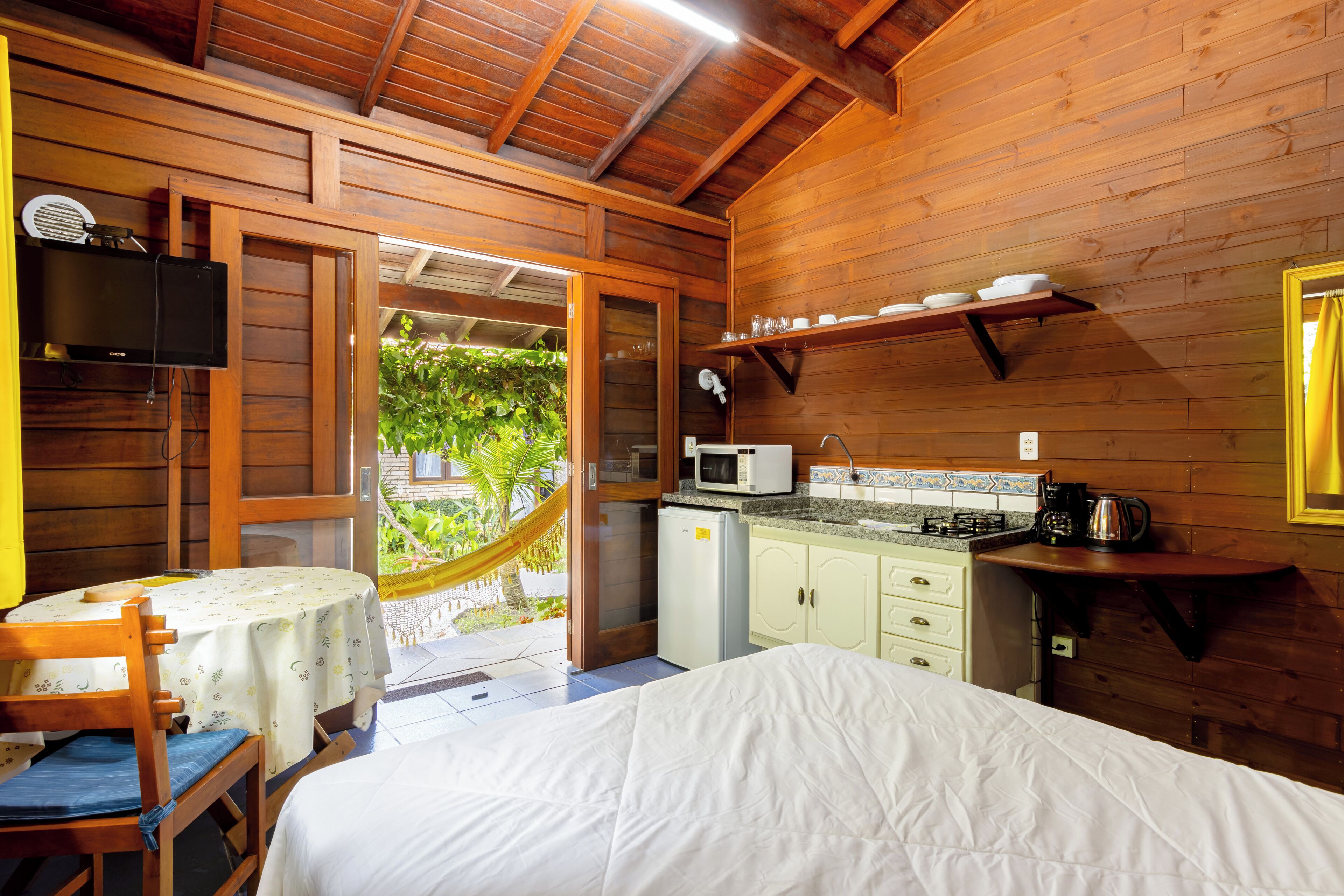 A wooden cabin with a bed, a small kitchenette, and a dining area with a table and chairs.