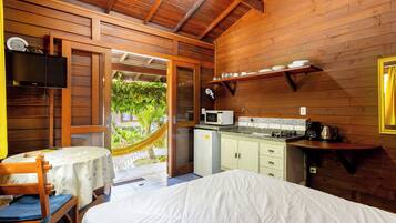 A wooden cabin with a bed, a small kitchenette, and a dining area with a table and chairs.