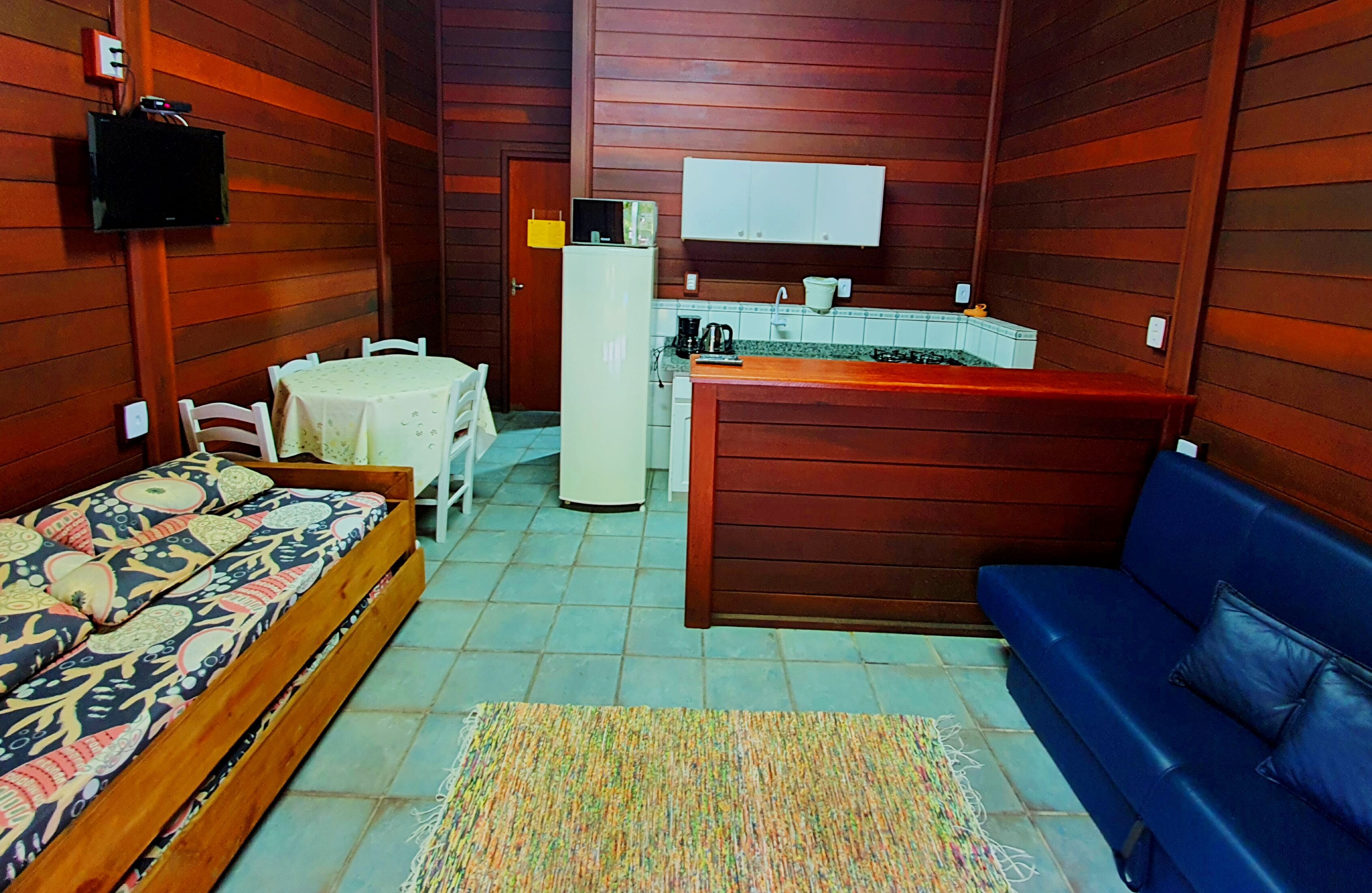 Una habitación compacta con cama, sofá, pequeña mesa de comedor, kitchenette y televisor.